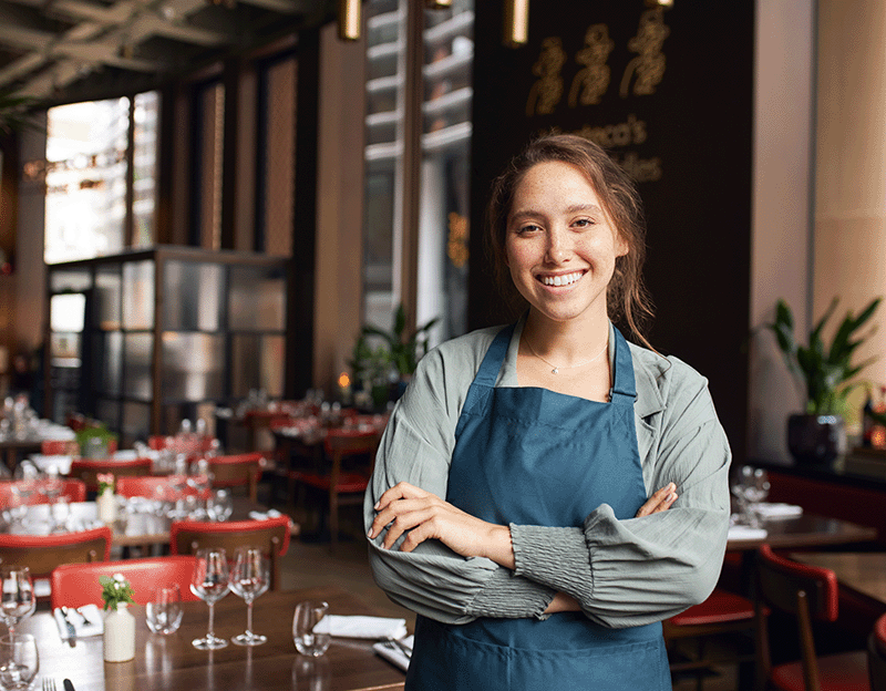 vrouw in horeca zaak met armen over elkaar lacht naar camera