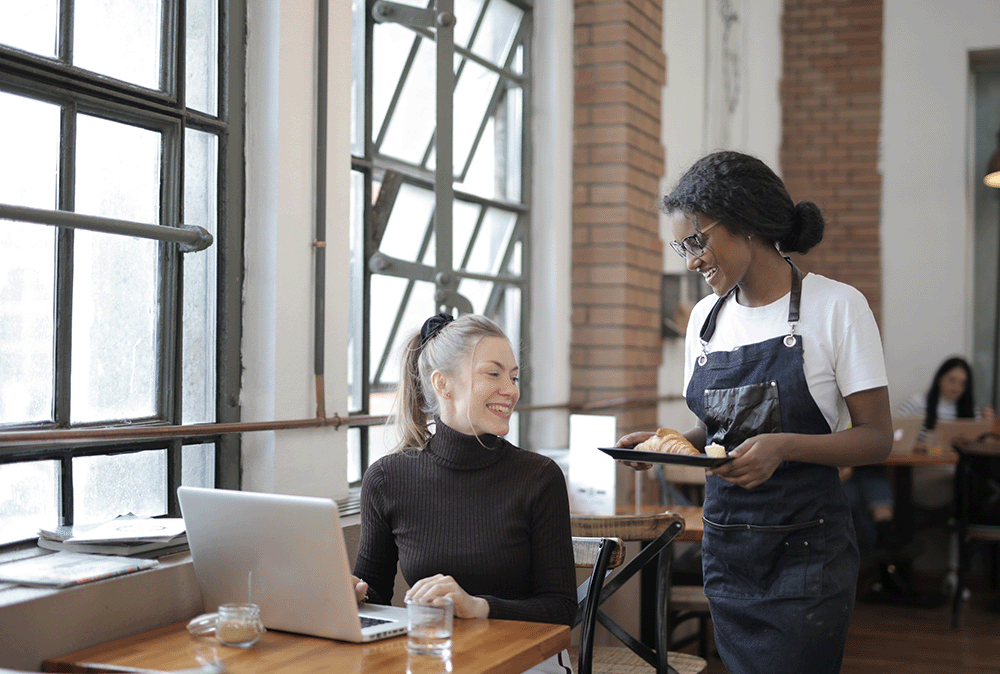 medewerker serveert croissant uit aan dame met laptop